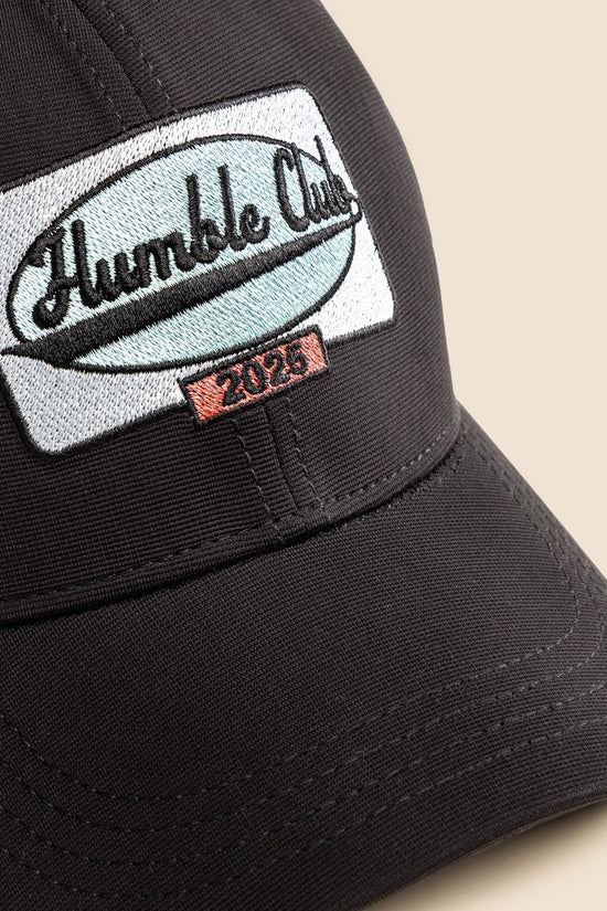 Black cap with 'Humble Club' logo on a beige background