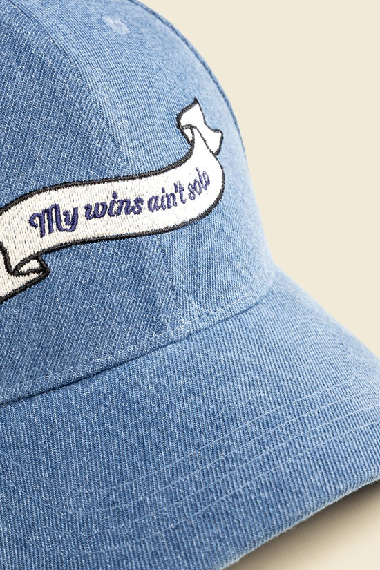 Blue denim cap with embroidered banner on a beige background