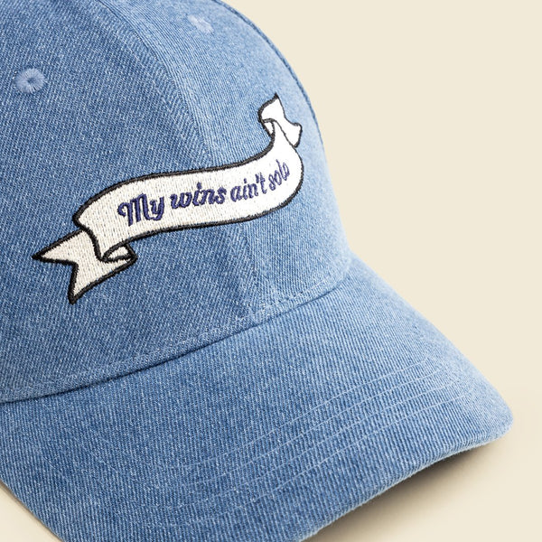 Blue denim cap with embroidered banner on a beige background