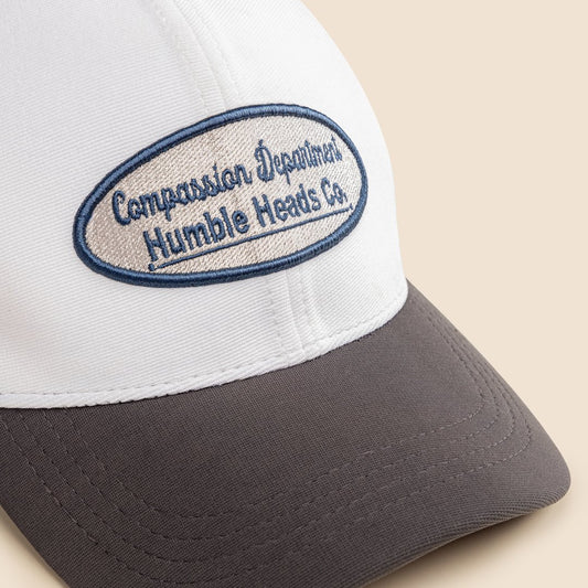 White and gray cap with a blue and beige embroidered patch on a beige background